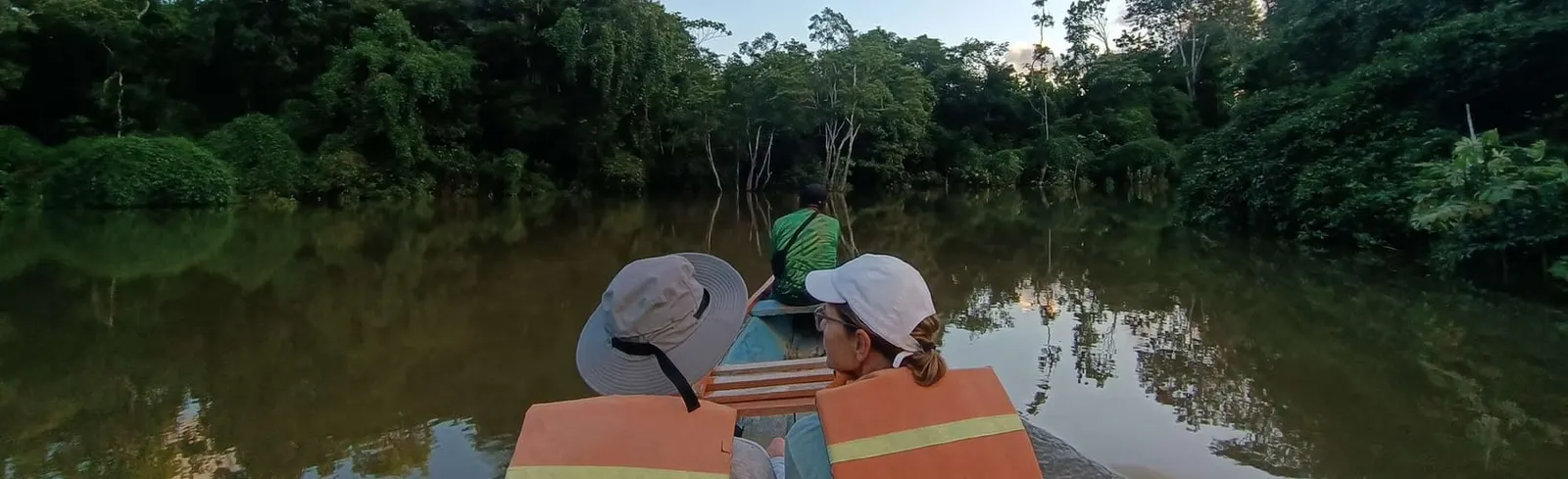 Two travelers in a canoe on a calm Amazon river surrounded by rainforest