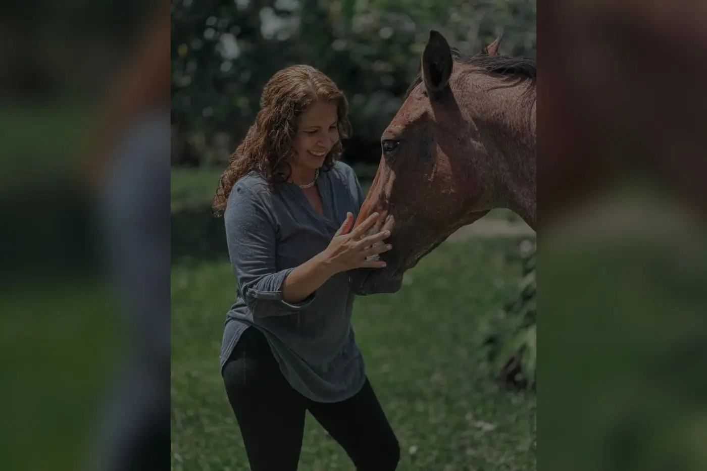 Woman gently touching a horse's face in a green meadow