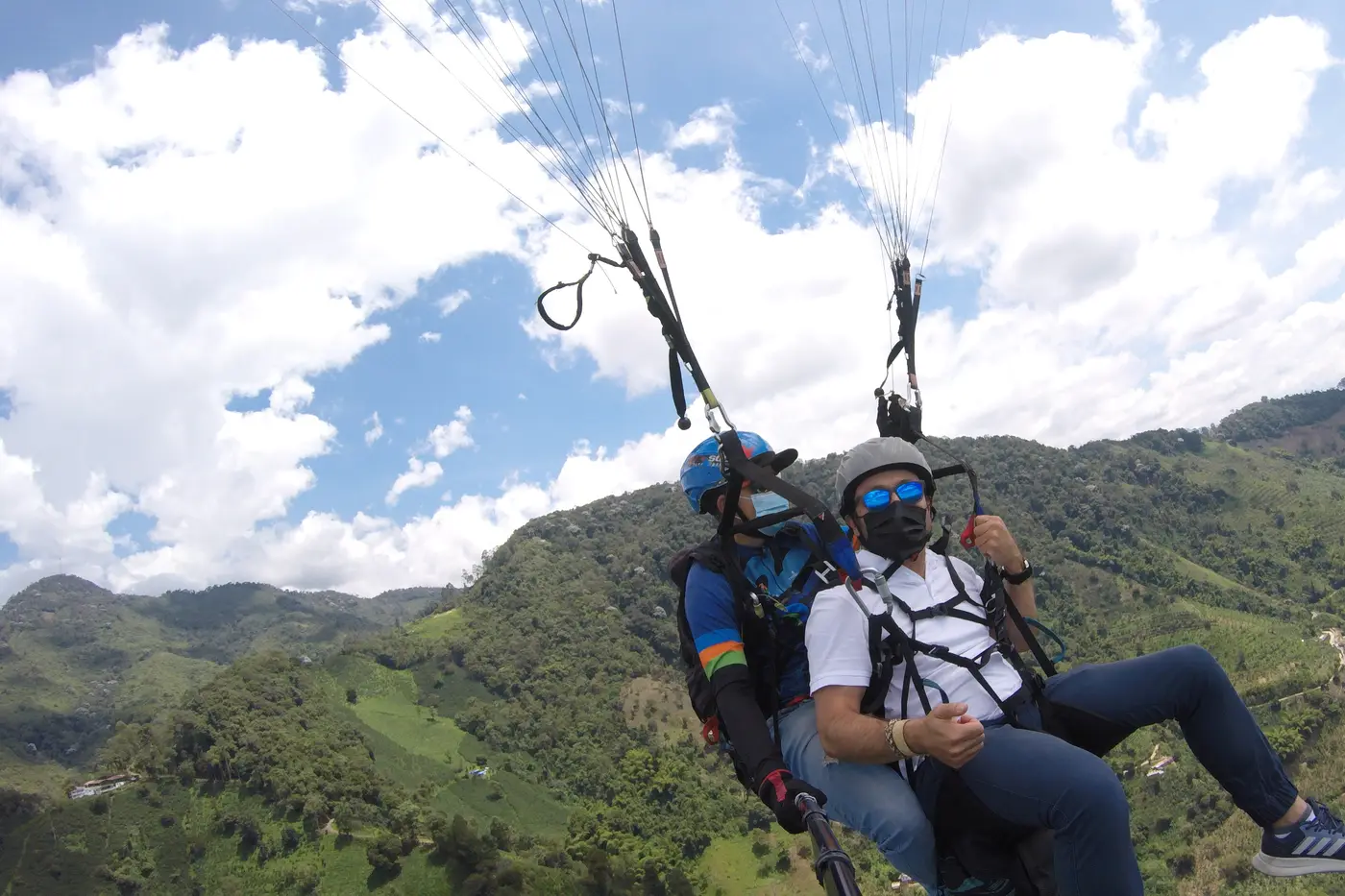 Tandem paraglider flying over green mountains in the Coffee Region