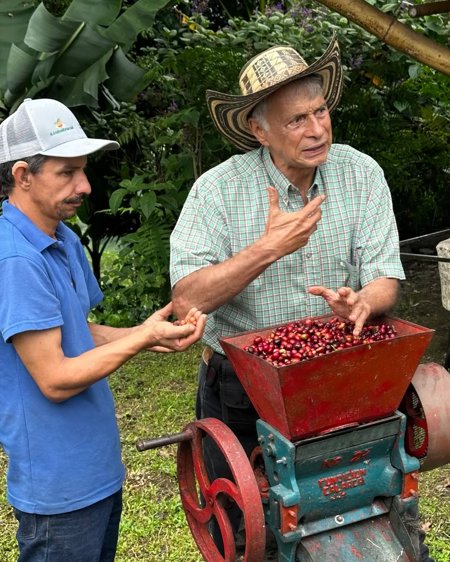 Two men beside a hand-cranked pulping machine filled with ripe red coffee cherries