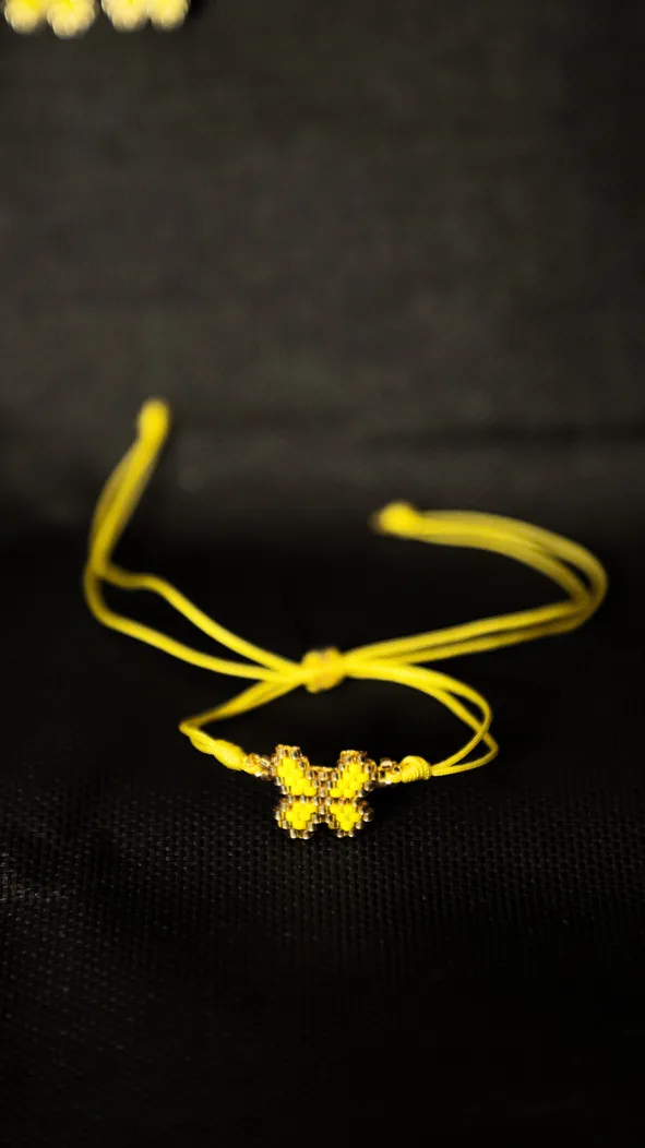Yellow butterfly bracelet with cords on a dark background