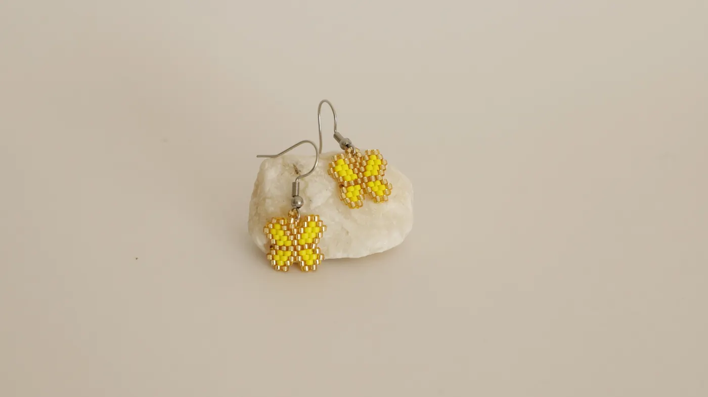 Pair of yellow beaded butterfly earrings resting on a stone