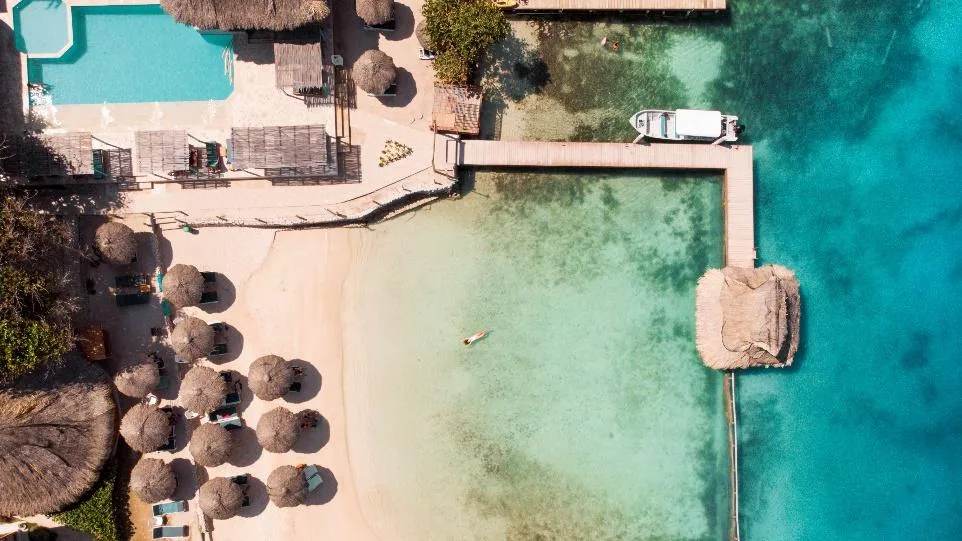 Vista aérea de la playa, las sombrillas y el muelle con kiosco de palma sobre el agua turquesa