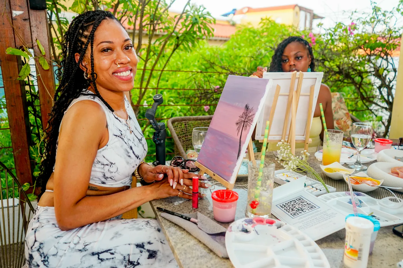 Two women painting on canvas at a leafy terrace in Cartagena