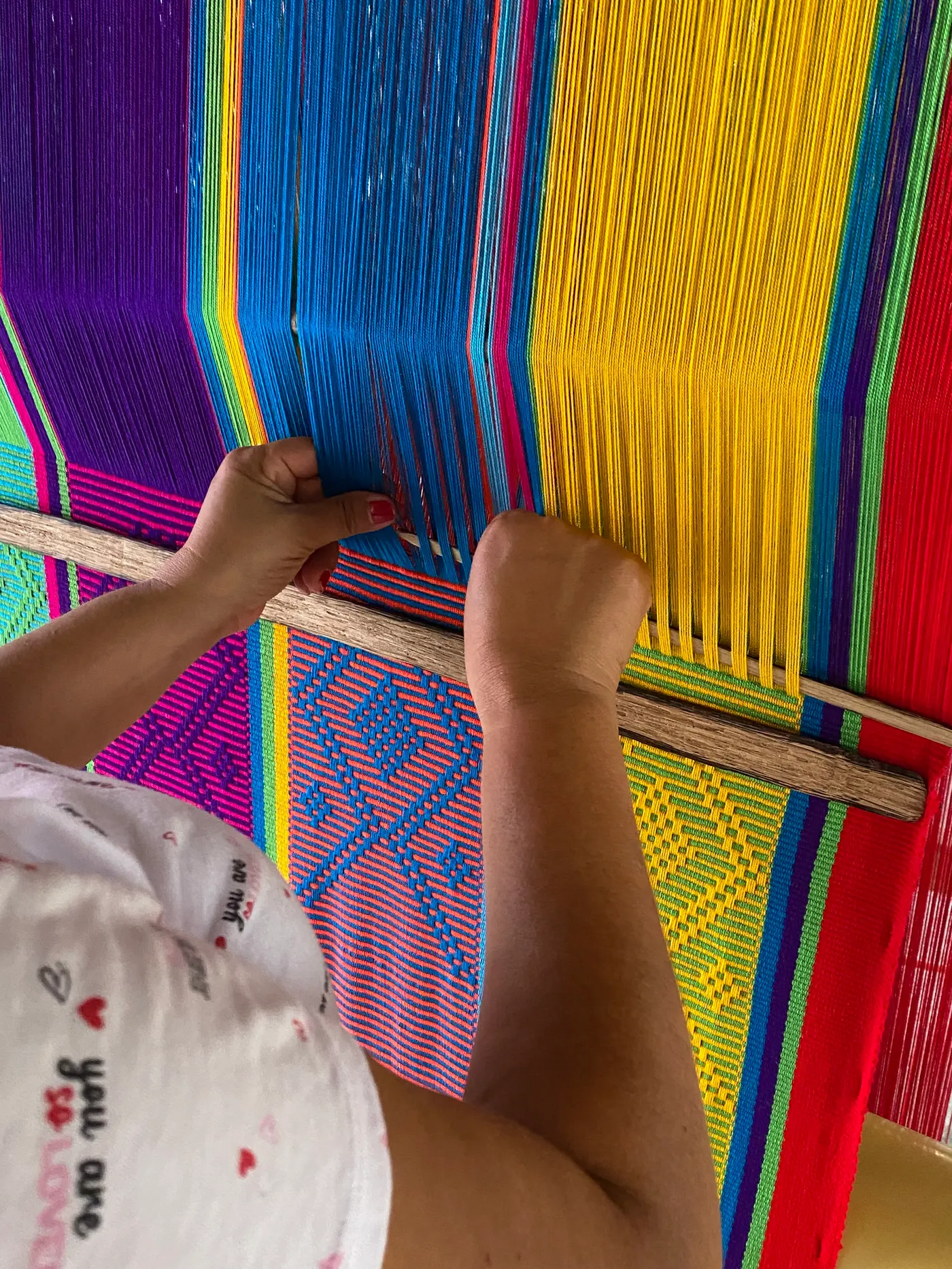 Hands weaving a colorful hammock on a wooden loom in San Jacinto