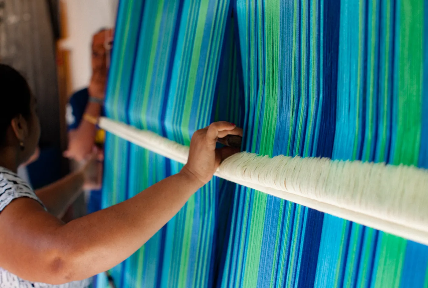 Weaver threading blue and green yarn on a hammock loom