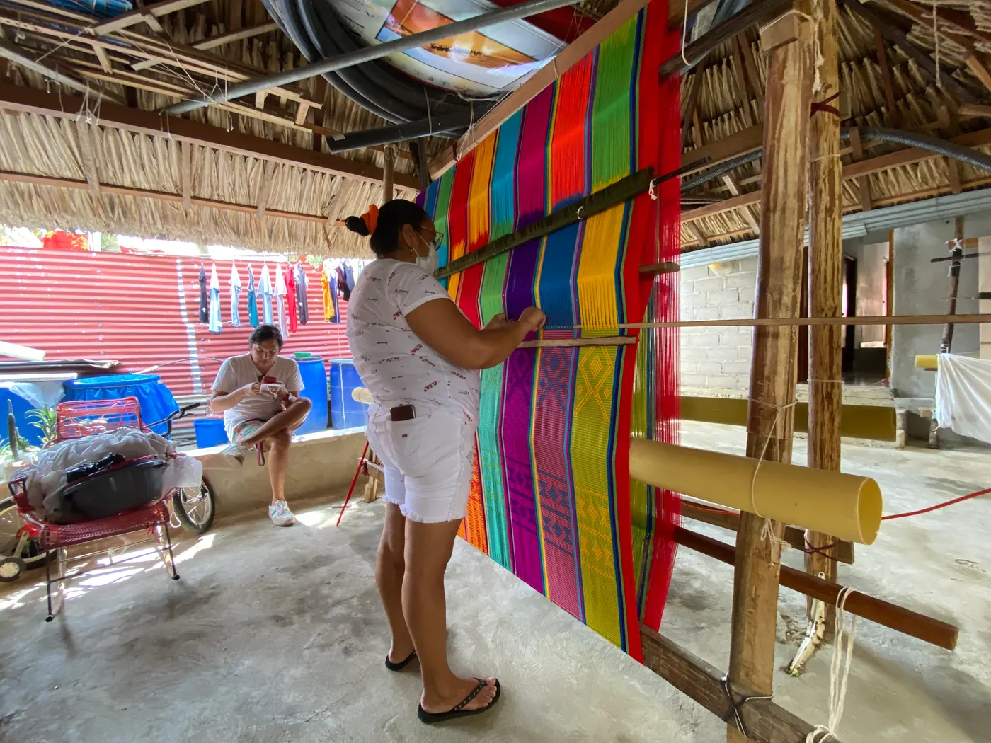 Weaver working at a large hammock loom in a workshop with colorful threads