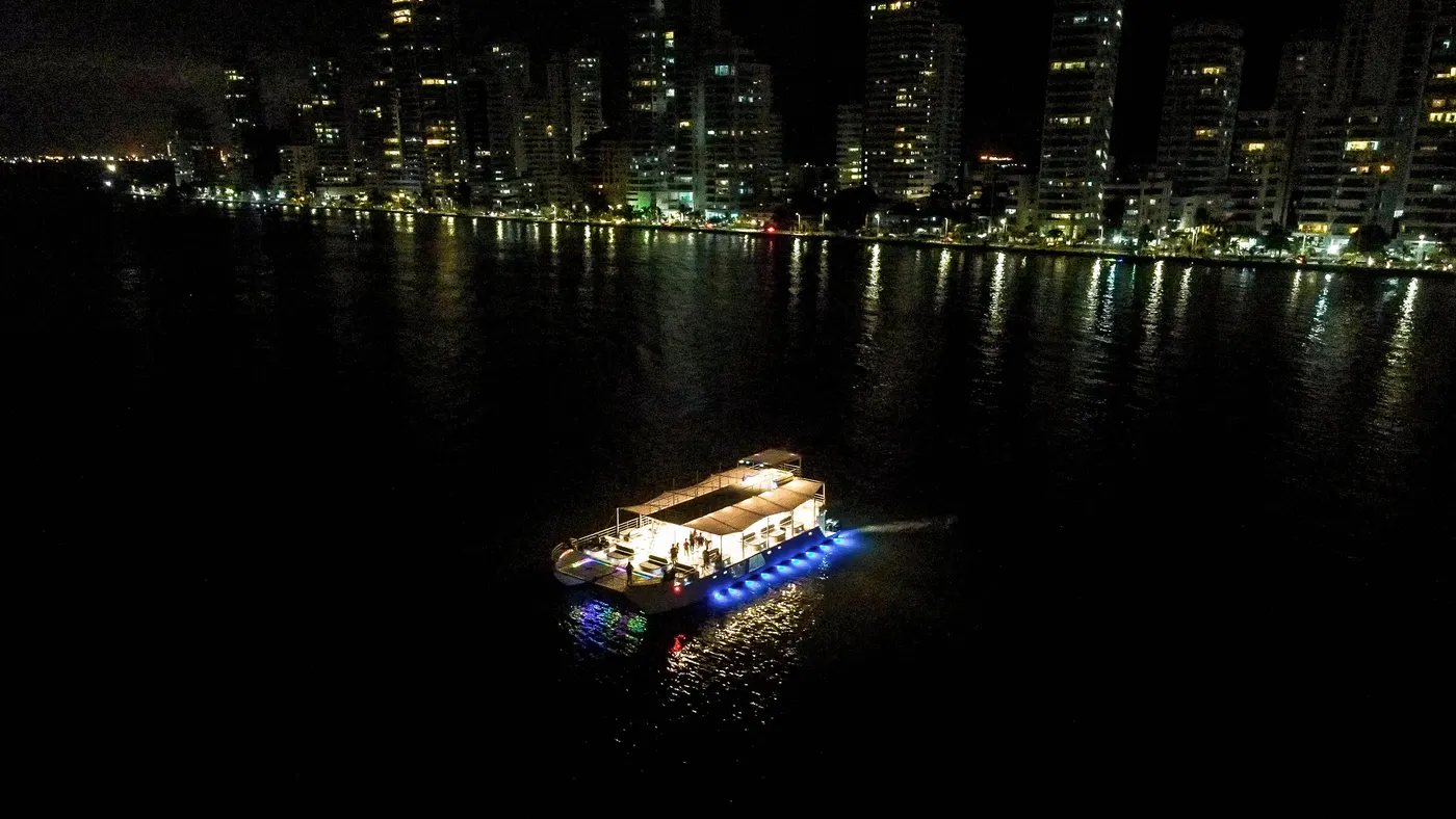 The catamaran lit up at night with the Cartagena skyline behind it