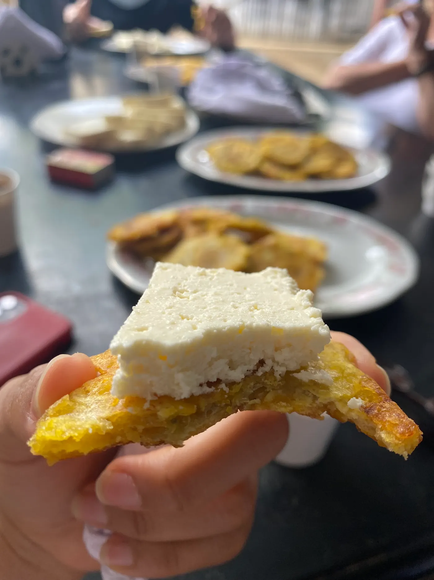 A hand holding a fried plantain topped with fresh white cheese
